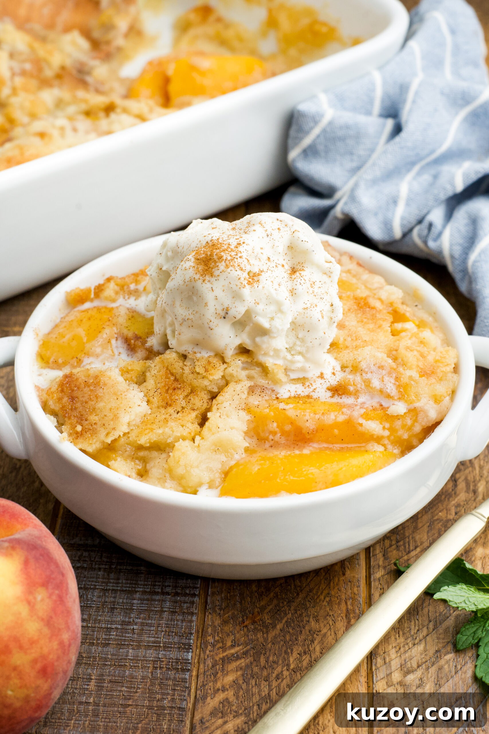 No-Bake Peach Dump Cake Recipe for Quick Summer Dessert 2 Front view of a serving of Peach Dump Cake in a white bowl topped with a scoop of vanilla ice cream.