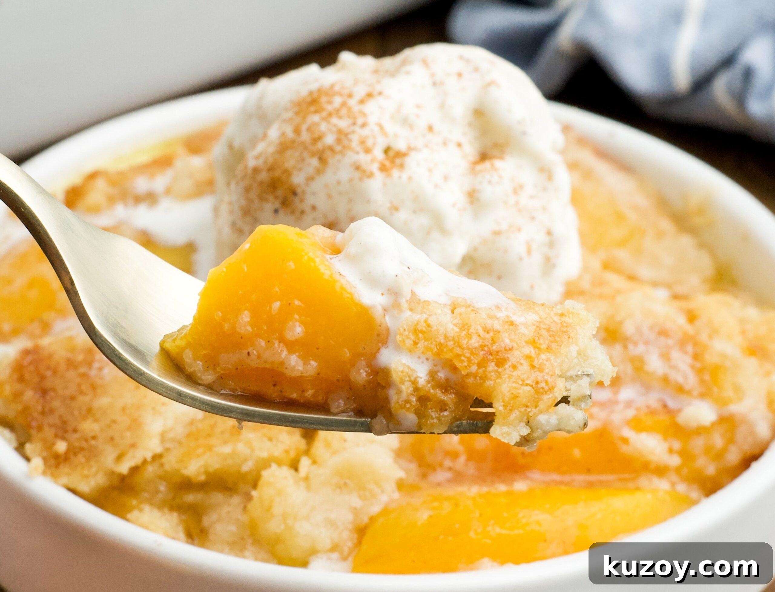 No-Bake Peach Dump Cake Recipe for Quick Summer Dessert 14 close up of of a serving of Peach Dump Cake in a white bowl with a gold fork removing a bite.