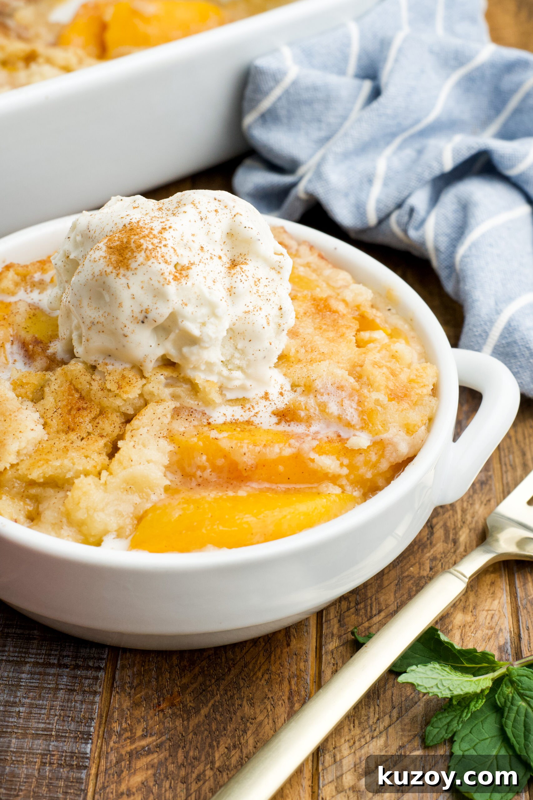 No-Bake Peach Dump Cake Recipe for Quick Summer Dessert 16 Front view of a serving of Peach Dump Cake in a white bowl topped with a scoop of vanilla ice cream.