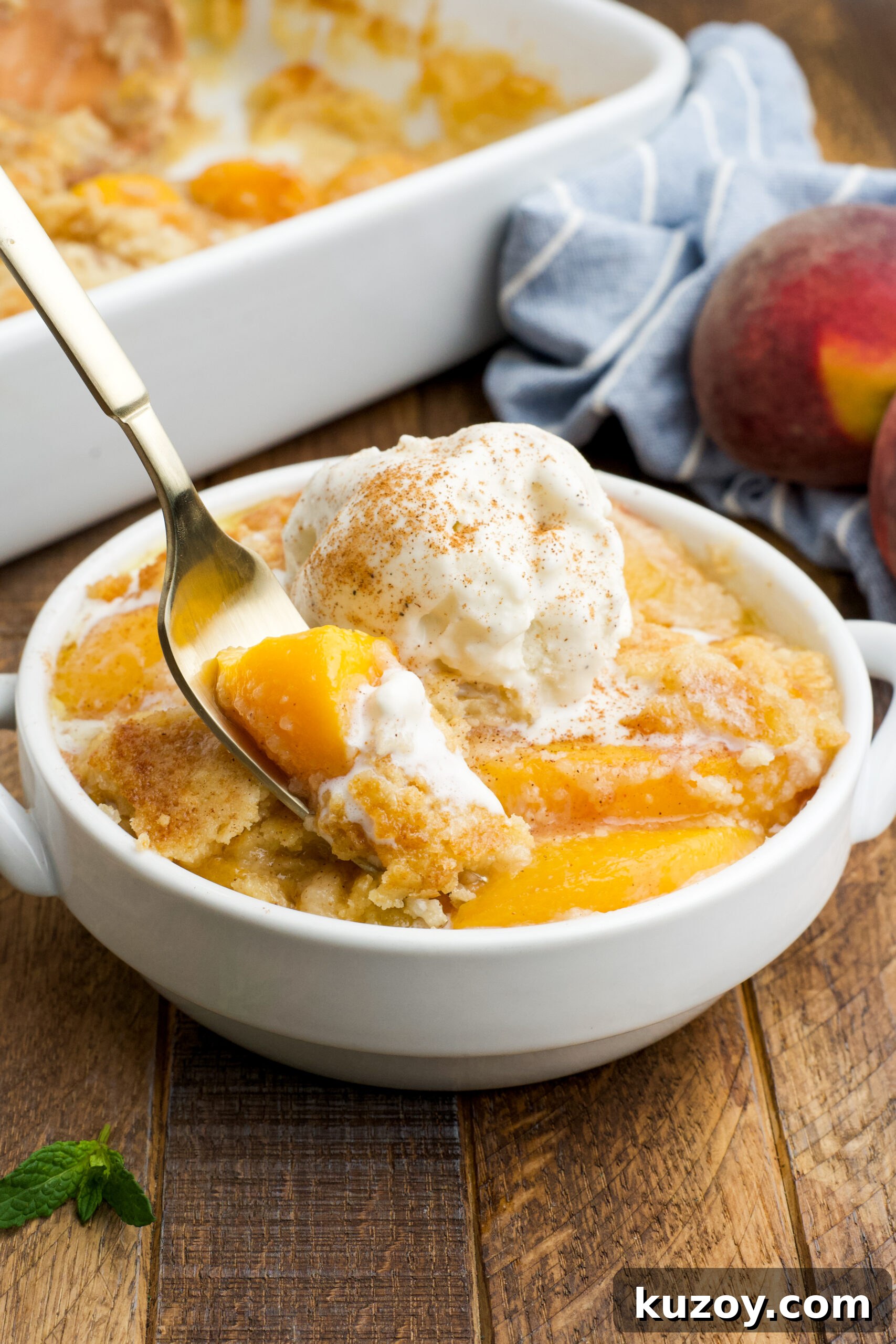 No-Bake Peach Dump Cake Recipe for Quick Summer Dessert 18 Front view of a serving of Peach Dump Cake in a white bowl with a gold fork removing a bite.