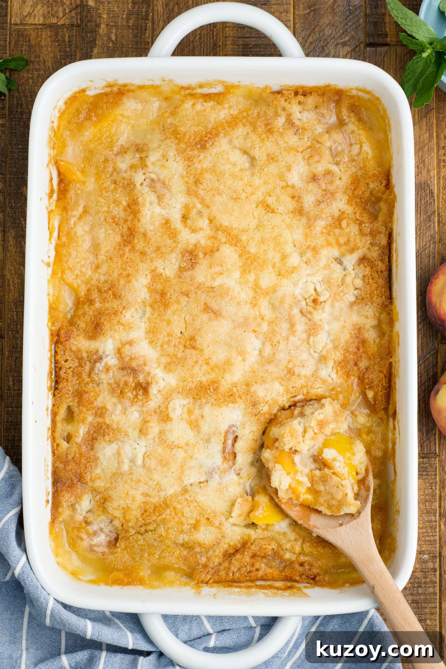 No-Bake Peach Dump Cake Recipe for Quick Summer Dessert 4 Overhead view of Peach Dump Cake in a white baking dish with a wooden spoon removing a serving.