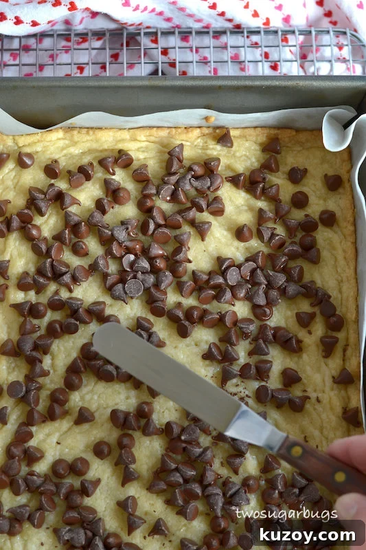 baked cookie base with softened chocolate chips being spread with an offset spatula