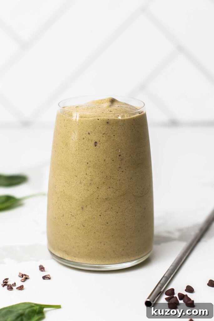 A green smoothie in a glass with a metal straw sitting next to it, showing the thick texture.