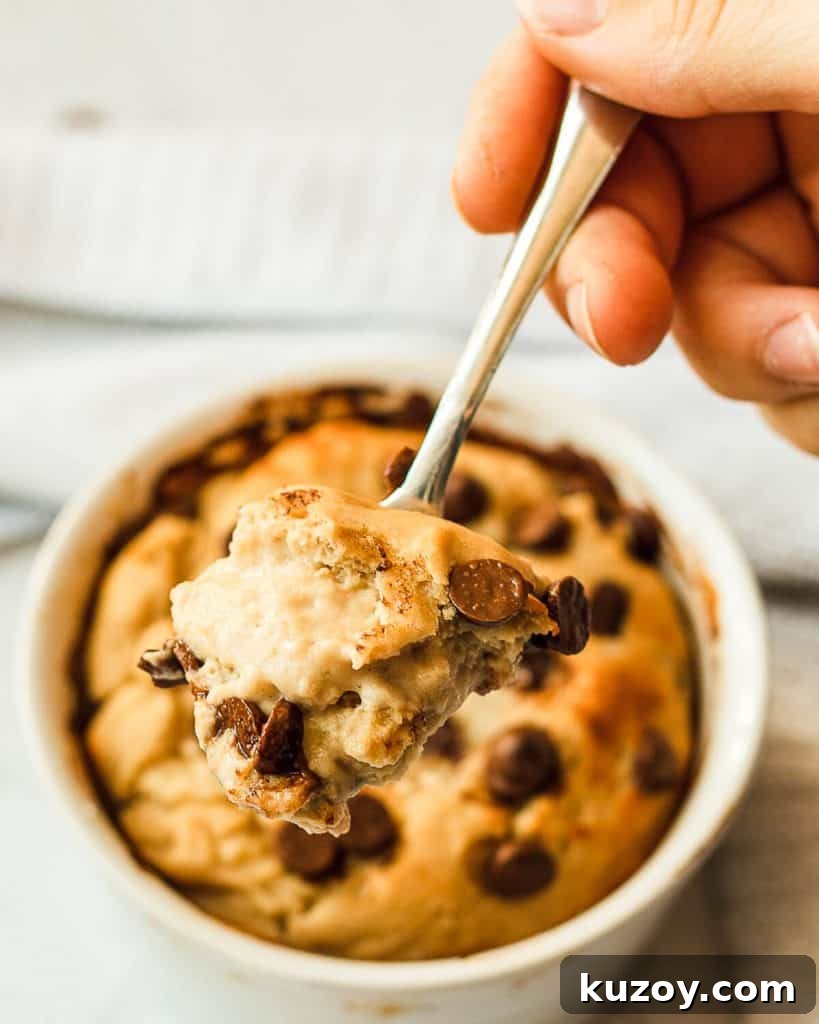 A close-up photo of a bite of gooey cookie in a mug, the cookie in a mug is out of focus in the background.
