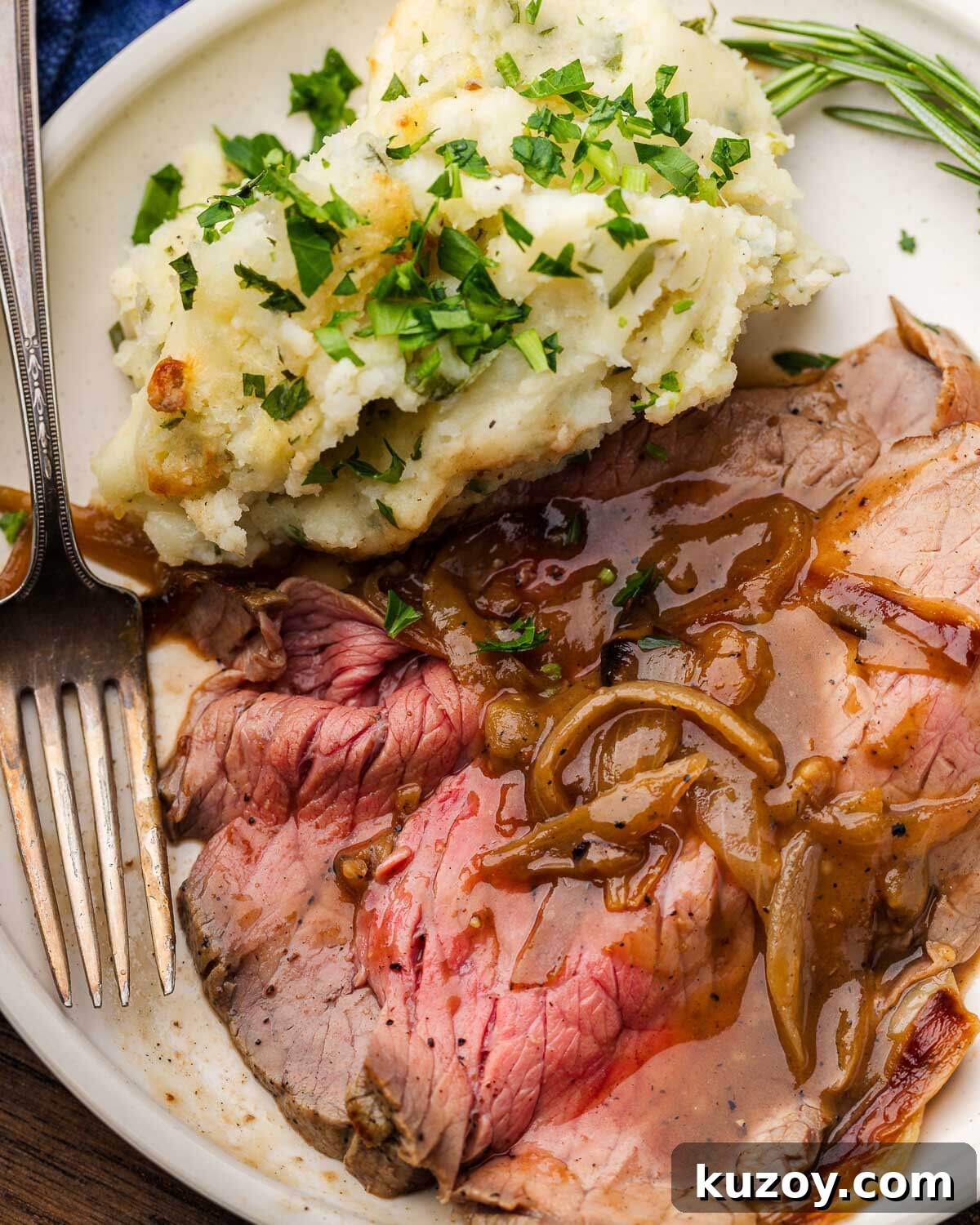 Rare slice of roast beef with onion gravy and mashed potatoes on white plate.