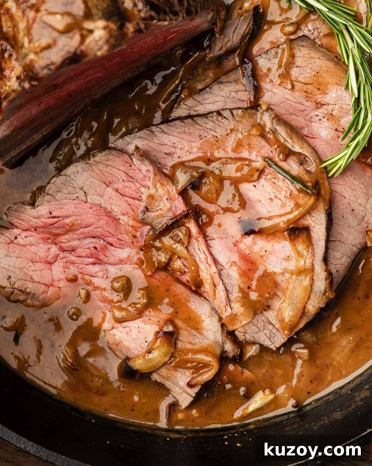 Sliced beef top round with onion gravy in cast iron pan.