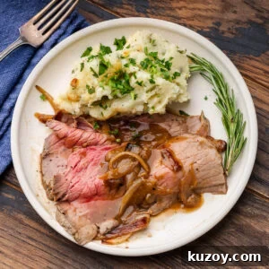 Sliced beef top round with onion gravy and mashed potatoes on white plate.