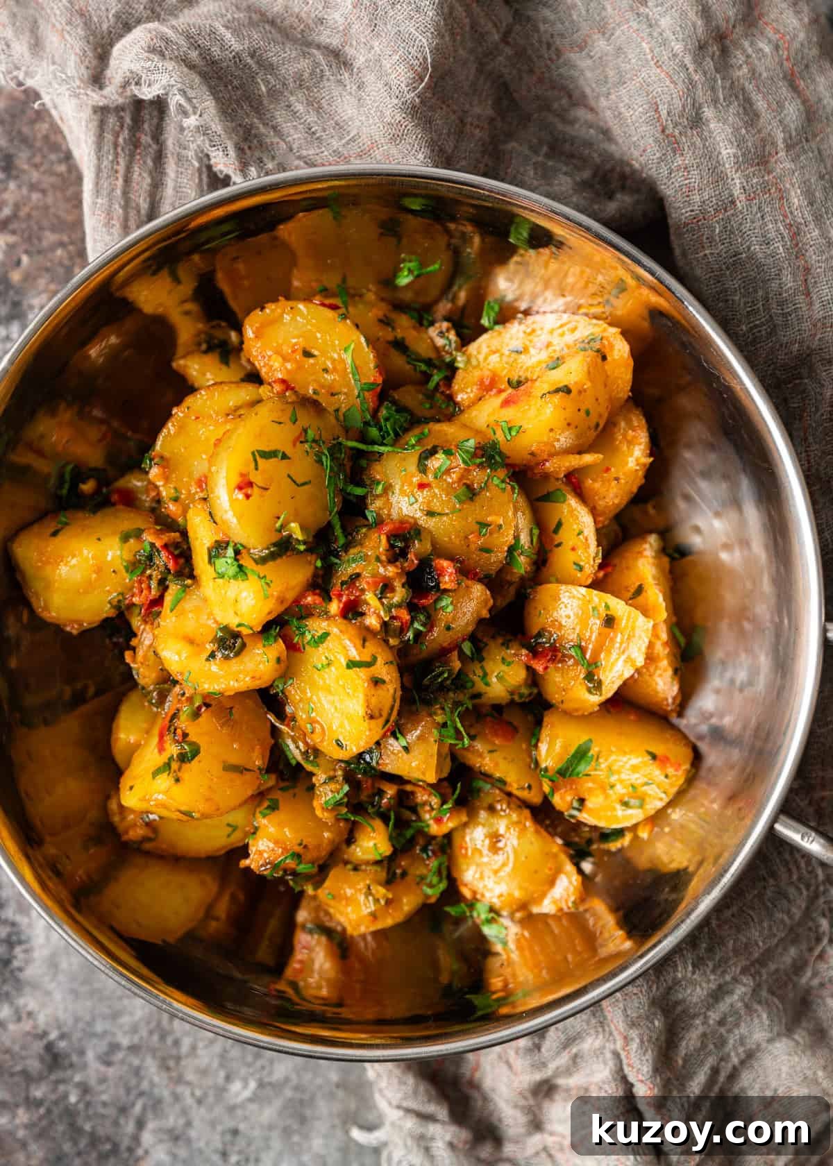 overhead: a metal bowl full of calabrian chili potatoes with herb butter