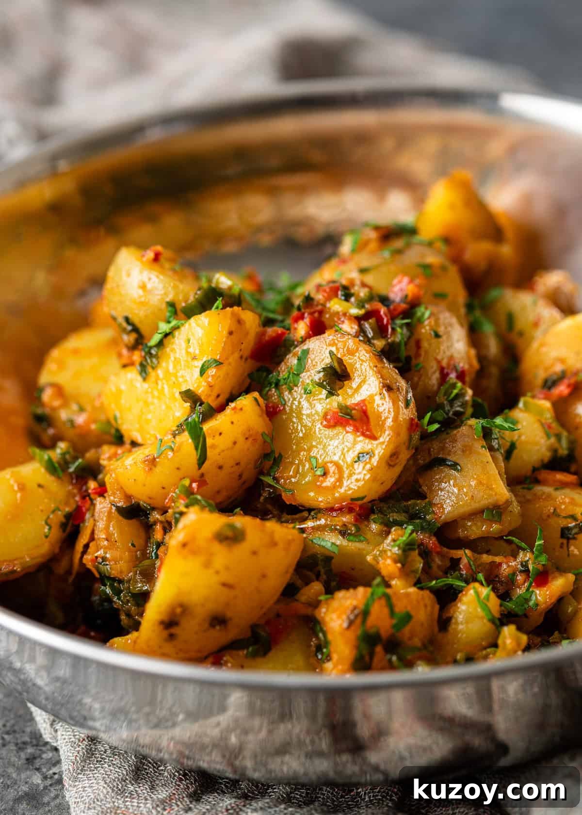closeup: calabrian chili potatoes topped with fresh chopped herbs in a metal bowl