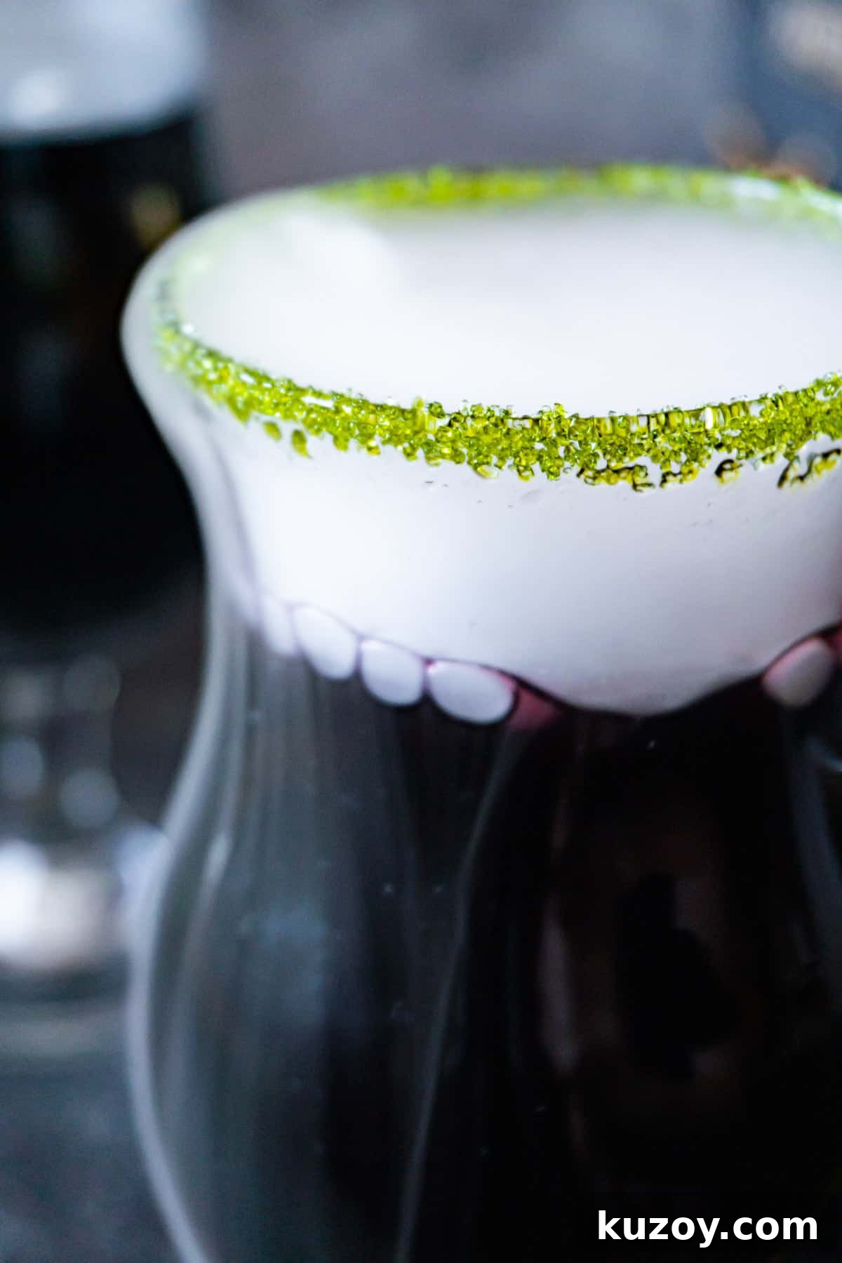 Spooky Cauldron Cocktail Recipe for Halloween Parties 2 black cauldron cocktail in a clear glass cup with a green sugared rim and with dry ice "smoke" spilling out.