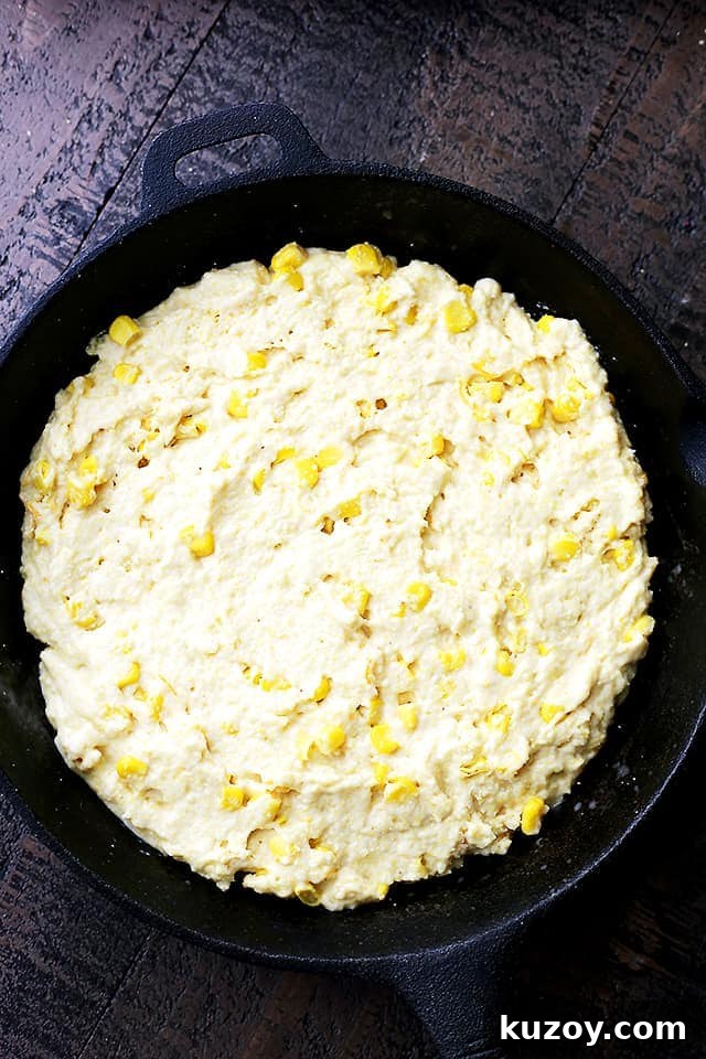 Loaded with fresh corn and a handful of cheddar cheese, this flavorful, lightened-up cornbread is the perfect side for your soup or chili! Cornmeal batter in a skillet with sweet corn and cheese, ready to be baked.