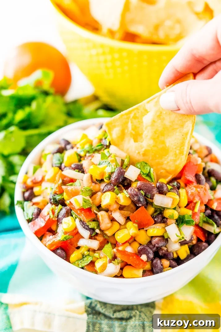 Zesty Cowboy Caviar Salad with Black Beans & Corn 4 Woman's hand dipping a tortilla chip into a bowl of Cowboy Caviar.