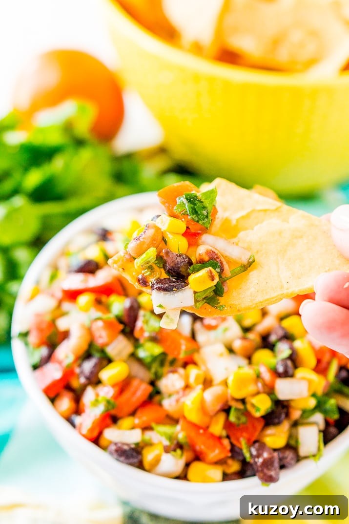 Zesty Cowboy Caviar Salad with Black Beans & Corn 5 Woman's hand holding a tortilla chip with a scoop of Cowboy Caviar on it.