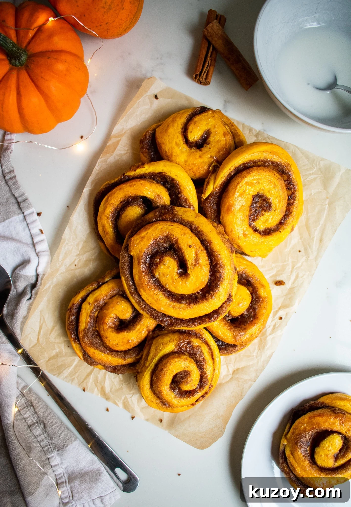 Pumpkin Spice Cinnamon Rolls with Spiced Sugar Glaze 2 Pumpkin cinnamon rolls on a piece of parchment paper.