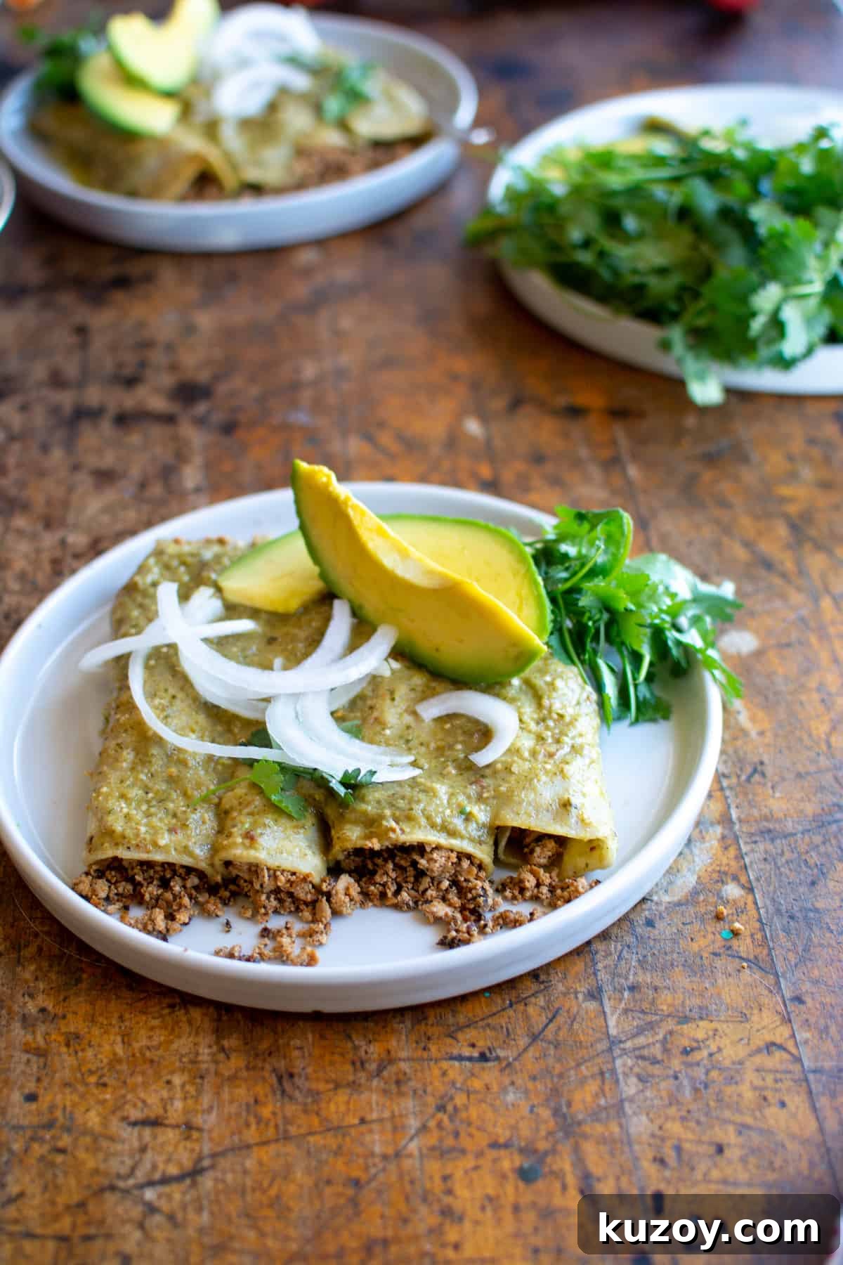 Four vegan enchiladas on a plate topped with sliced white onions and avocado.