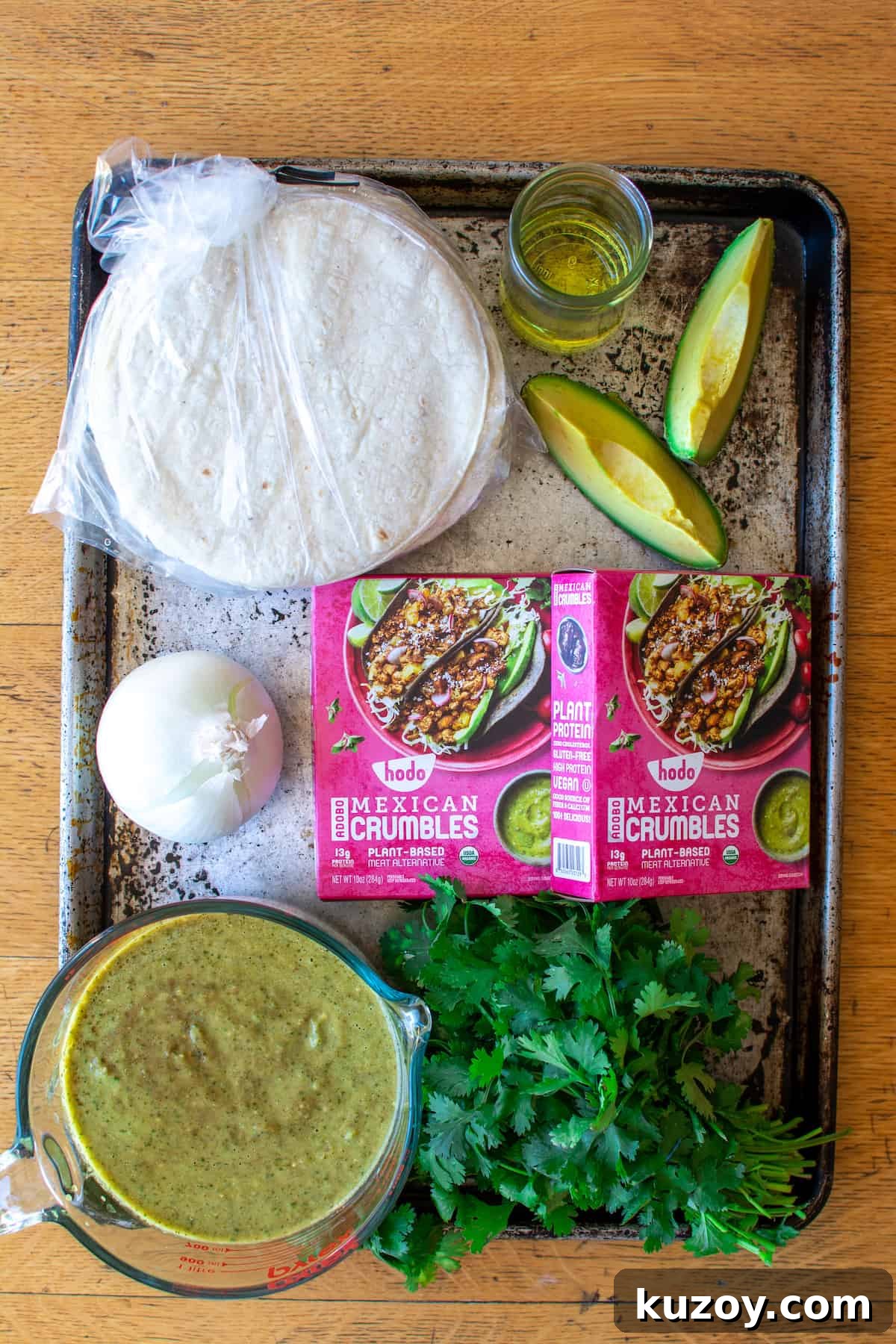 All the ingredients to make this vegan enchilada recipe sitting on a baking sheet on a wood table. Tortillas, avocado, and oil.