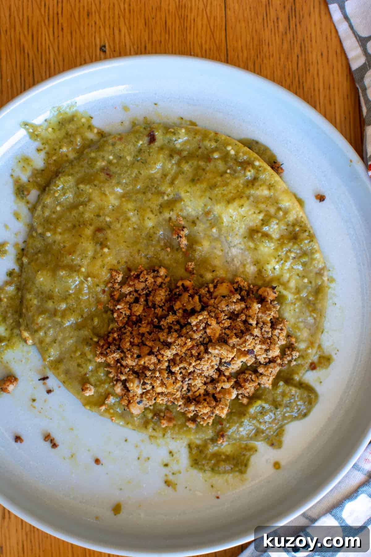 A tortilla soaked in Tomatillo Red Chili Sauce and topped with Hodo Adobo Mexican Crumbles about to get rolled up into an enchilada.