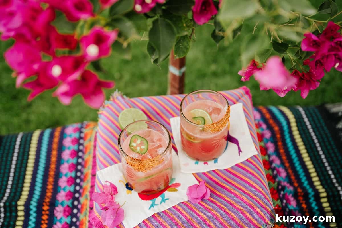 Spicy Jalapeño Watermelon Mezcal Margarita Recipe 7 overhead shot of 2 watermelon mezcal margaritas garnished with jalapeno slices on a colorful table under a flower bush.