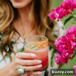 Spicy Jalapeño Watermelon Mezcal Margarita Recipe 8 Latina blogger holding a tajin-rimmed jalapeno watermelon margarita near a flower bush.