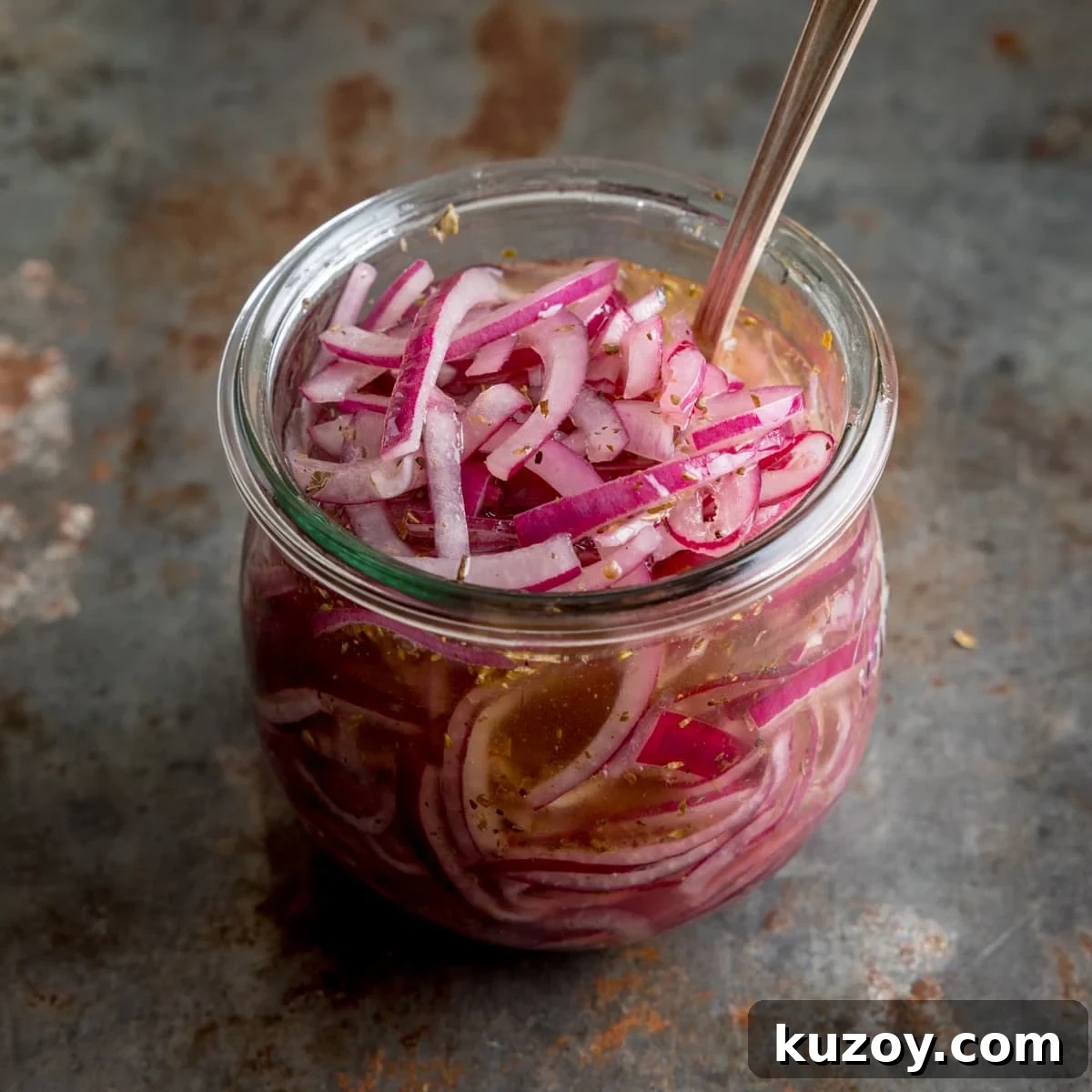 Creamy Avocado Toast with Lemon, Chili Flakes, and Crispy Sourdough 5 Marinated sliced red onions in a glass jar with a metal spoon sticking out. The jar is on a vintage steel surface.