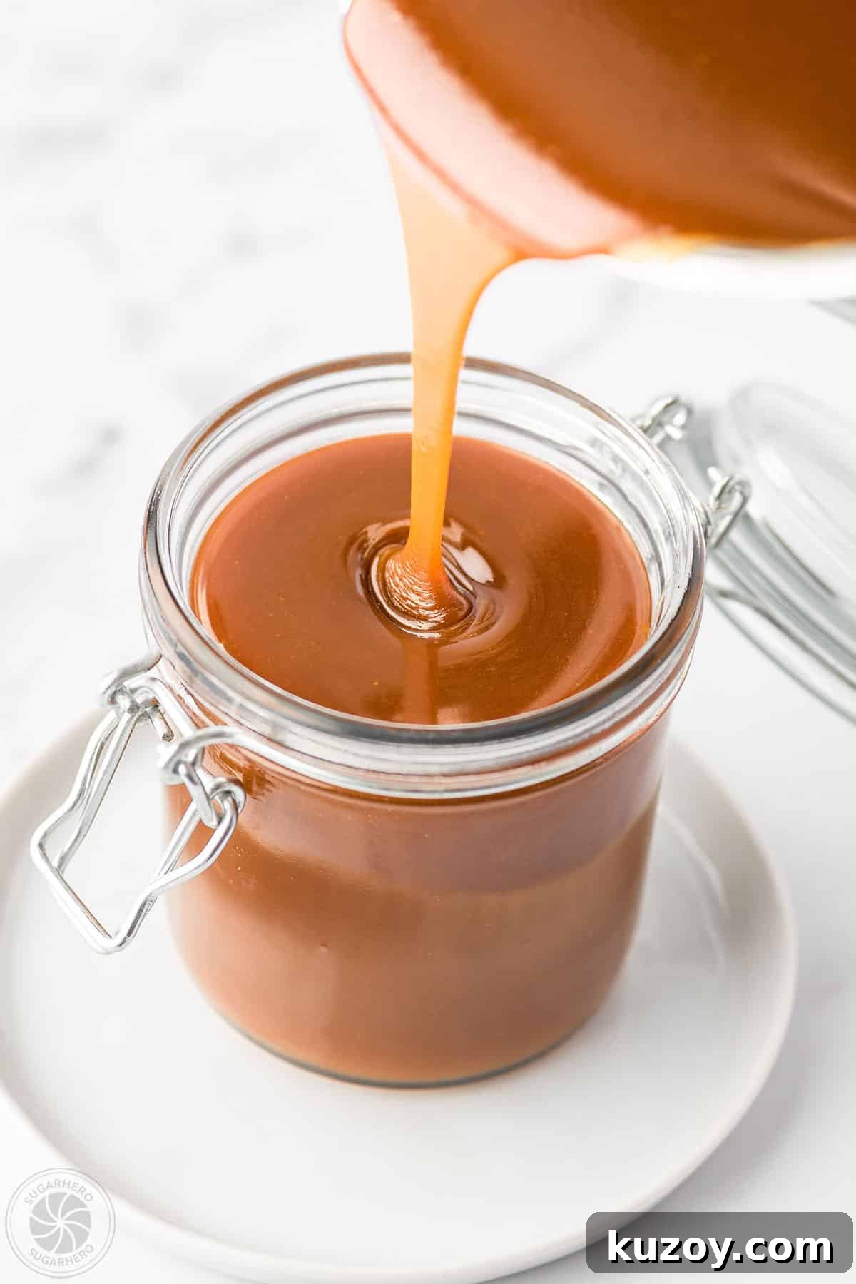 How to Make Smooth Homemade Caramel Sauce for Desserts 2 Pouring caramel sauce into a glass jar that is placed on a white plate.