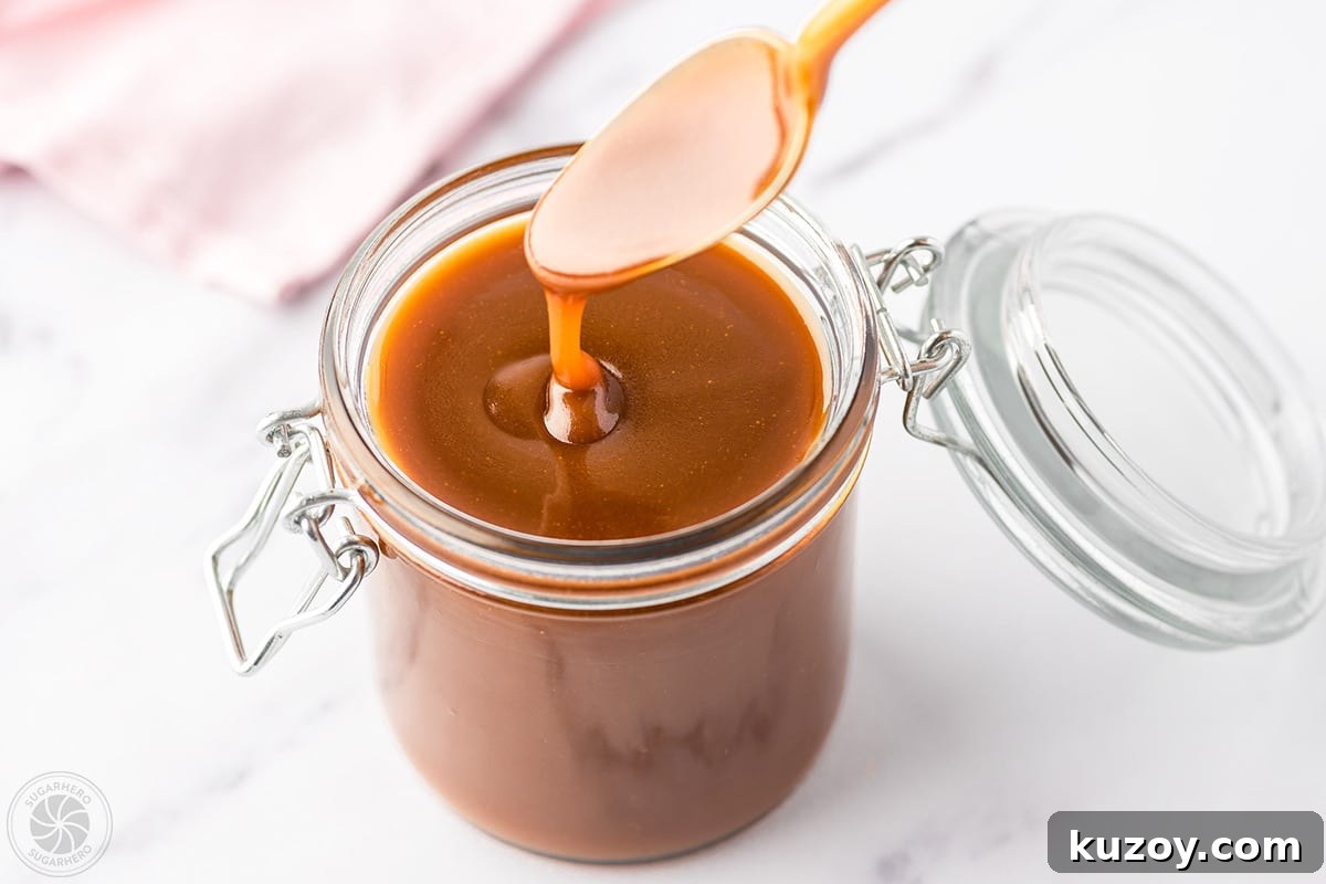 How to Make Smooth Homemade Caramel Sauce for Desserts 16 A glass jar full of caramel sauce with a spoon dripping in caramel sauce hovering over the jar.
