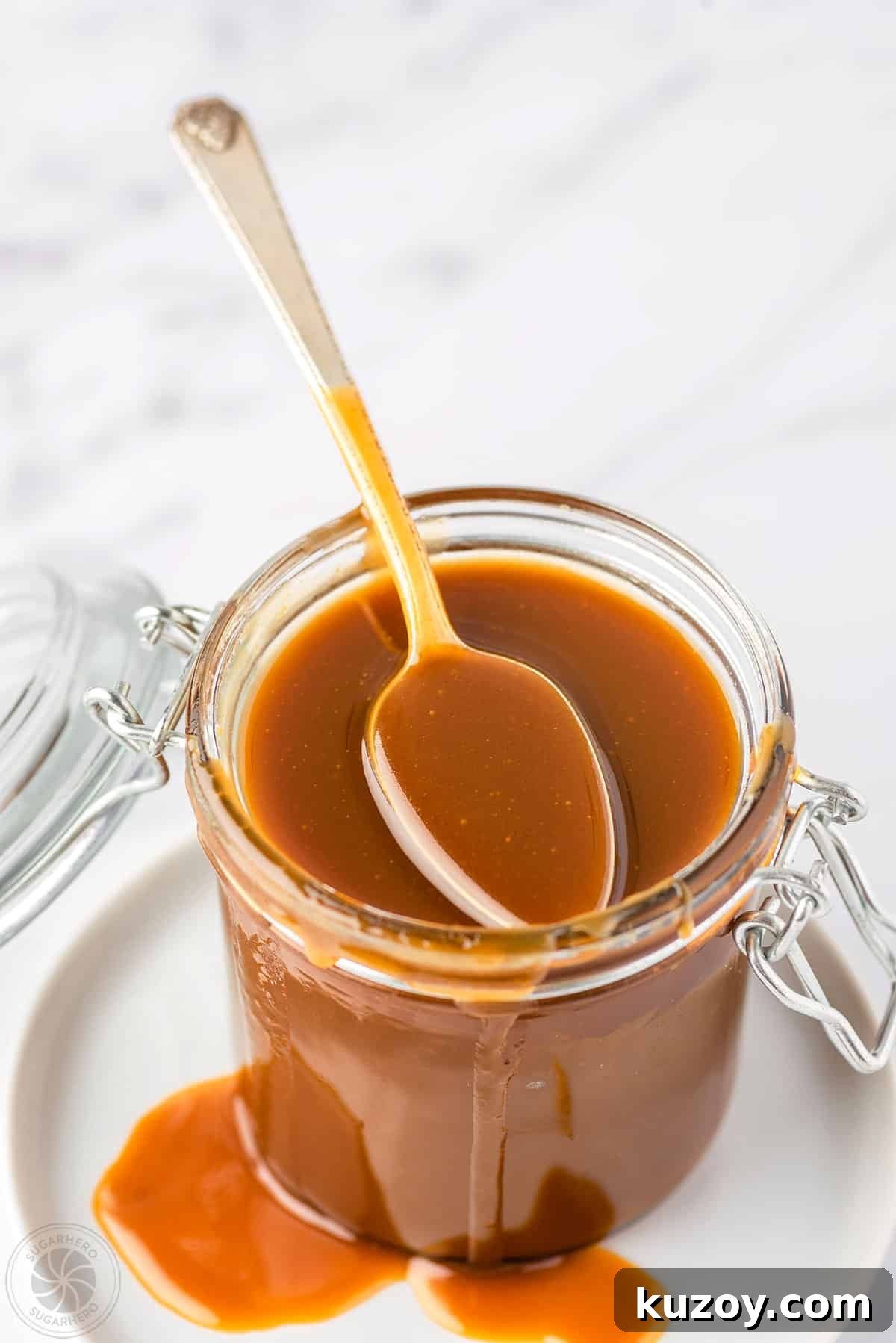 How to Make Smooth Homemade Caramel Sauce for Desserts 17 A spoon with caramel sauce on it sitting on the top of an open glass jar full of caramel sauce.