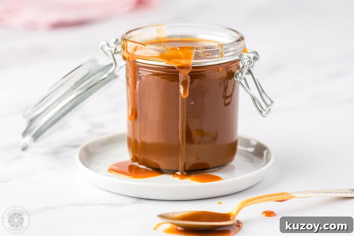 How to Make Smooth Homemade Caramel Sauce for Desserts 4 A glass jar full of caramel sauce with sauce also dripping down the sides of the jar and on the spoon set beside the jar.