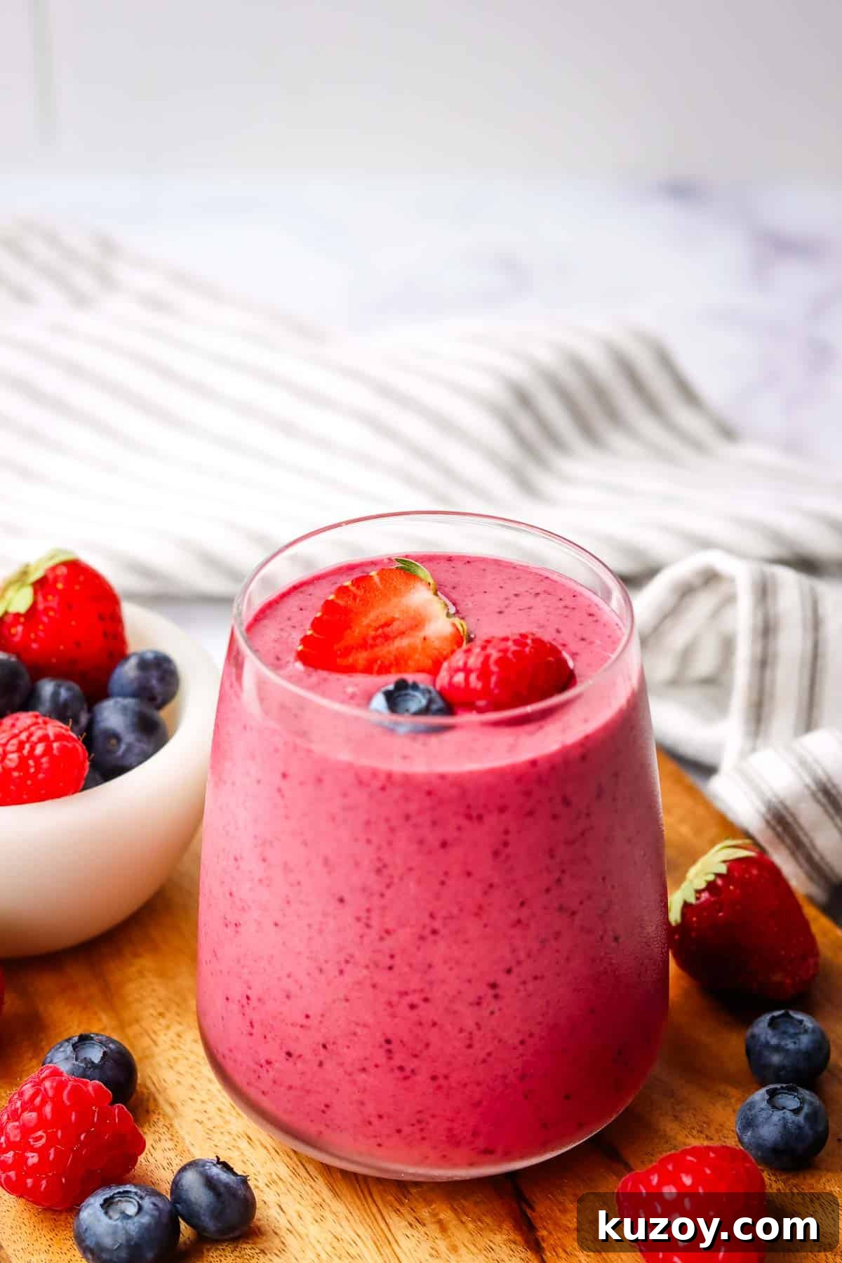 a glass of triple berry smoothie garnished with strawberries and blueberries