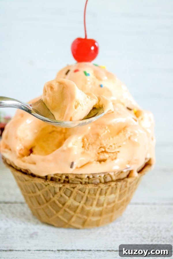 Orange Creamsicle Ice Cream Recipe: Creamy Orange Vanilla Scoop 2 a spoon lifting out a bite or orange creamsicle ice cream from a waffle cone bowl.