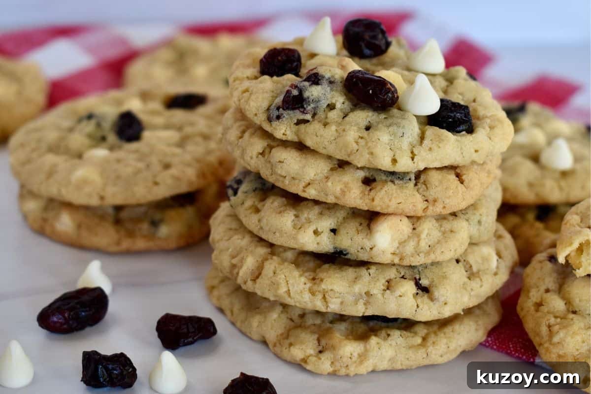 White Chocolate Craisin Oatmeal Cookies Recipe 3 Stack of oatmeal craisin cookies on a counter with a checkered napkin in the background.