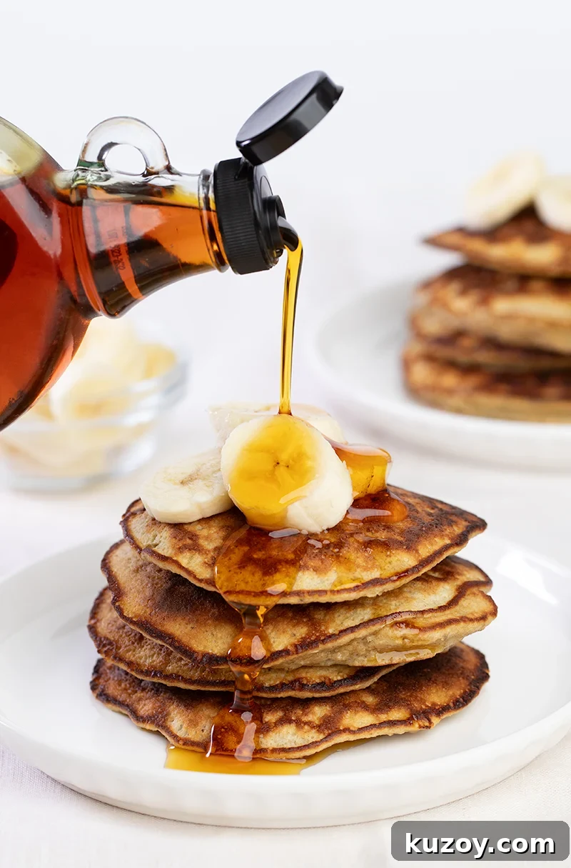 A stack of gluten free banana pancakes with syrup pouring from a bottle onto them.
