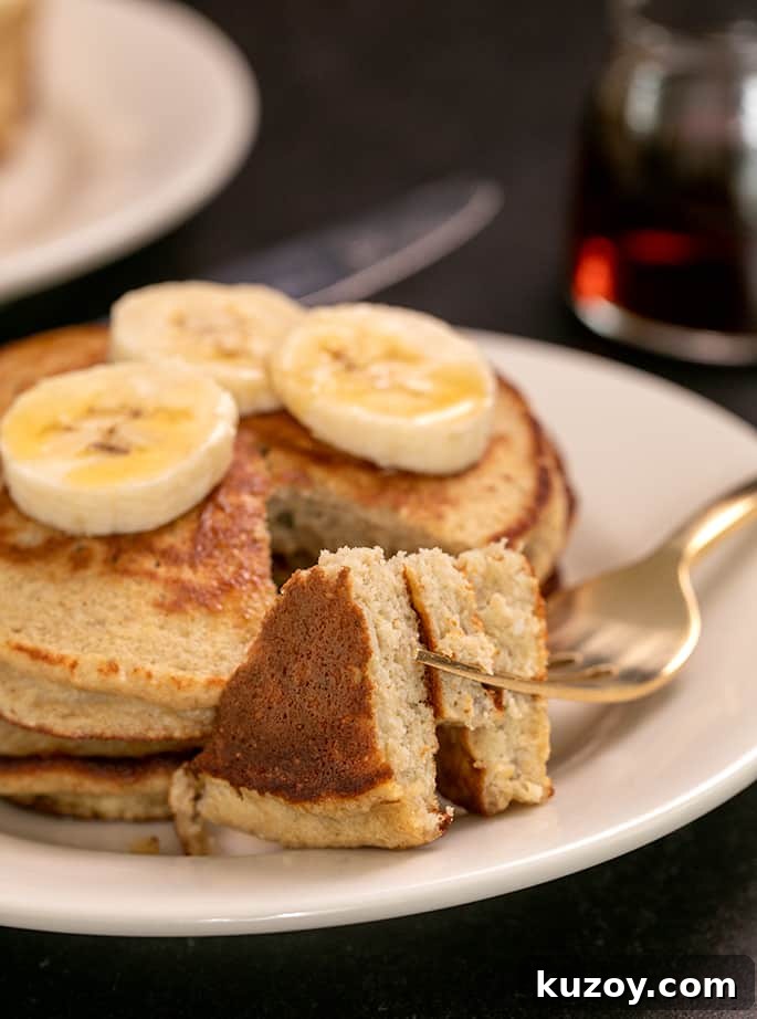 Fork with bite of 3 banana pancakes on a small white plate