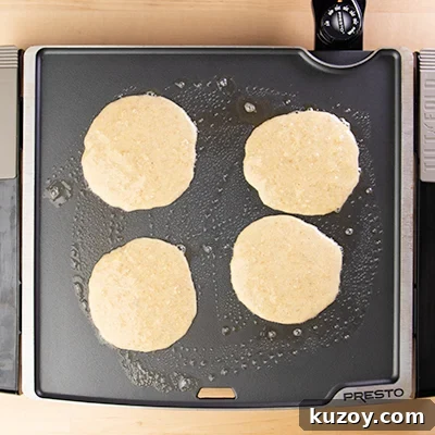 Four pancakes on the griddle cooking.