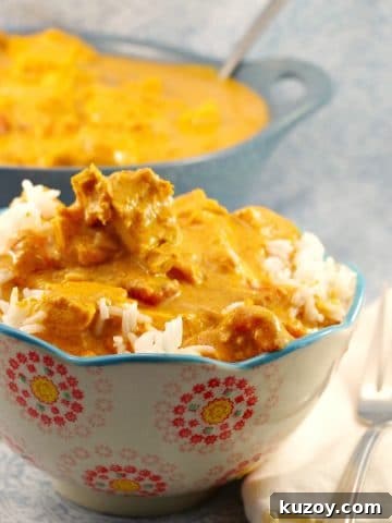 butter chicken in a patterned bowl with fork on the side and pot of healthy butter chicken in the background