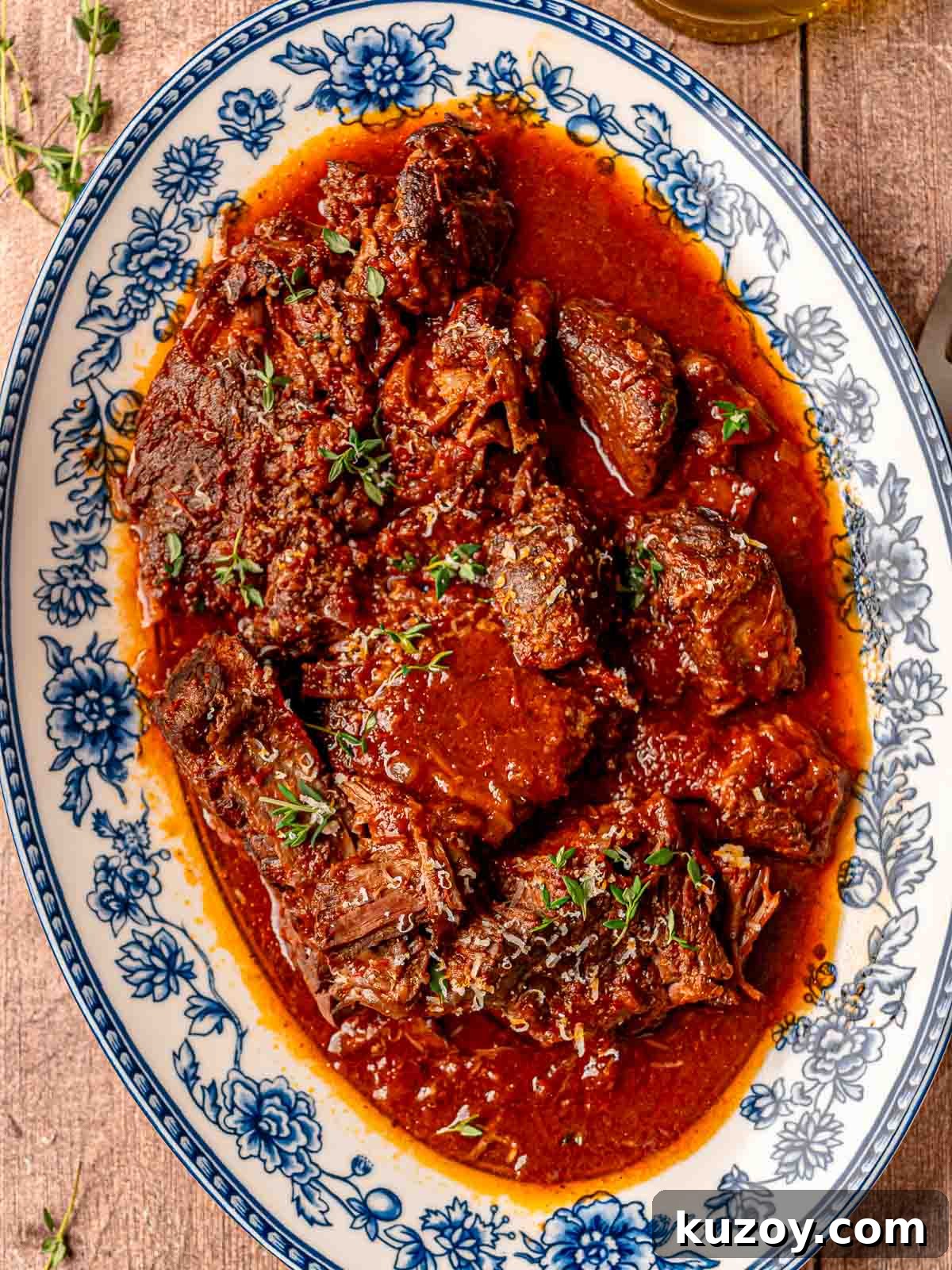 Italian pot roast pieces on a floral platter with tomato gravy, Parmesan, and fresh thyme.