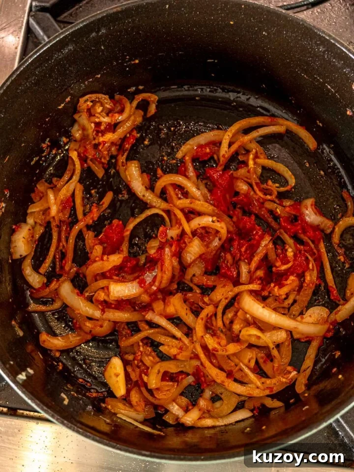 Sliced onions, garlic, and tomato paste sautéing in the bottom of a Dutch oven.