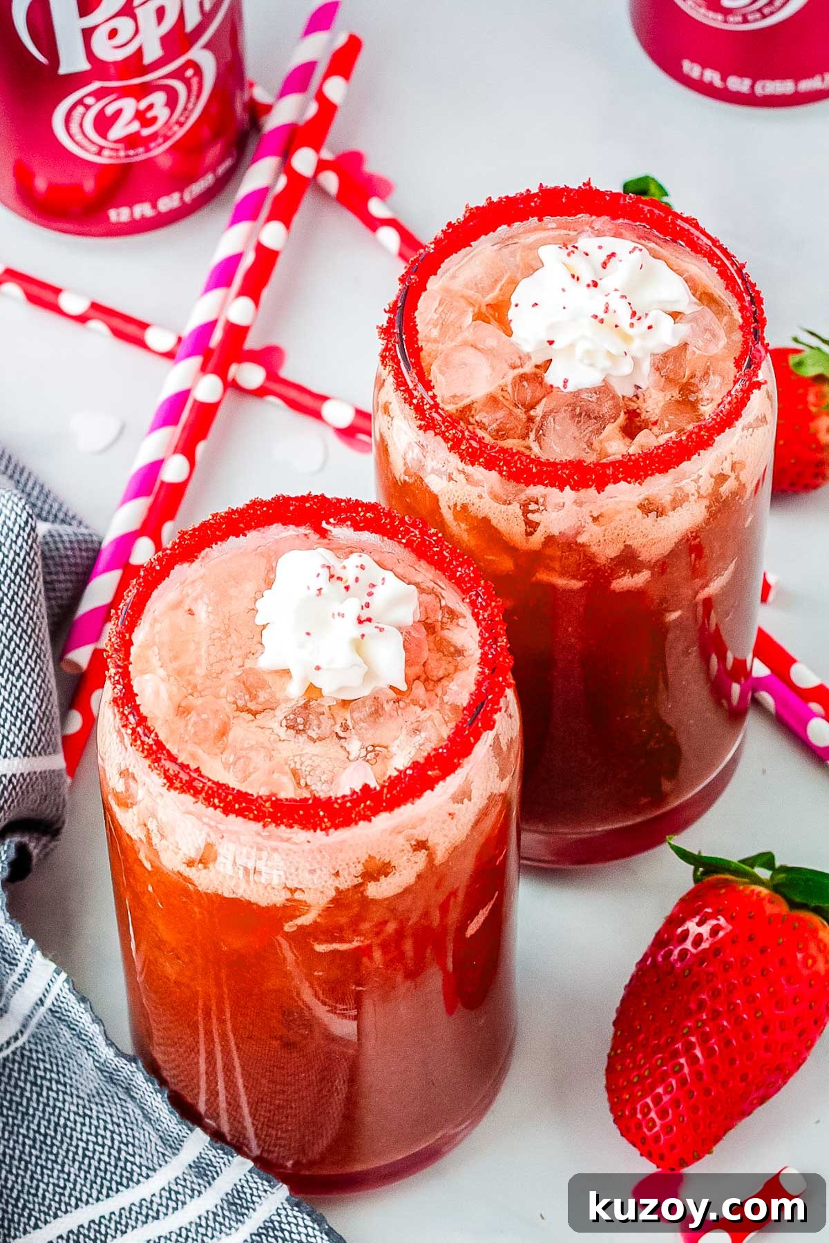 Swig Spring Fling Copycat Drink Recipe for Valentine’s Day 6 Valentine’s Day strawberry dirty Dr Pepper drinks in clear glasses with pebble ice, red sugar rims, whipped cream, and fresh strawberries on a white surface.
