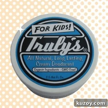 A top view of Truly's all natural cream deodorant for kids with a blue, black, and white label. The background is a graphic of duotone of white and beige dots.