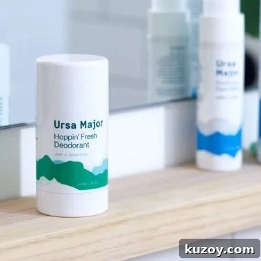 A stick of Ursa Major's Hoppin' Fresh vegan deodorant stick on a wooden shelf in front of a mirror with another Ursa Major product in the background.