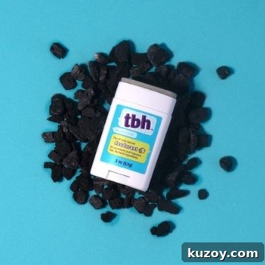 A flatlay of TBH Kids activated charcoal deodorant stick is open on top of a pile of charcoal on a light blue background.