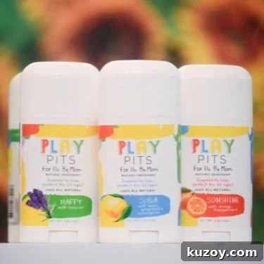 Three natural deodorant sticks from Play Pits. The scents are "Happy" "Suga" and "Sonshine". Blurry sunflowers are in the background.