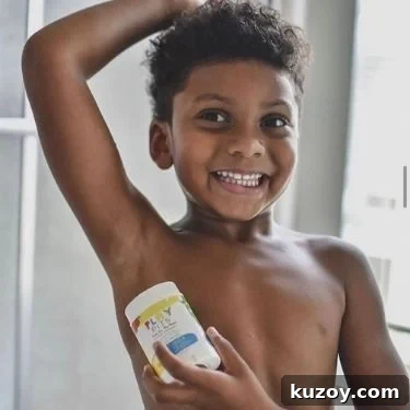 A young child with dark skin and short dark hair is smiling and looking at the camera while applying a Play Pits natural deodorant stick to their underarm.