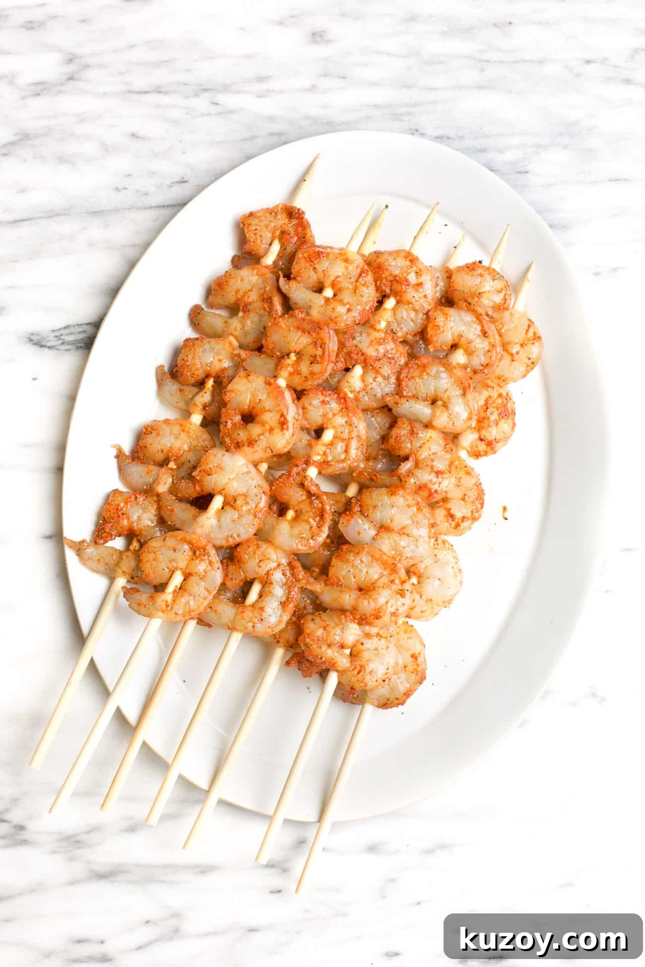 Spicy Cajun Shrimp Skewers with Garlic Butter Dip 4 seasoned raw shrimp kabobs on a white plate