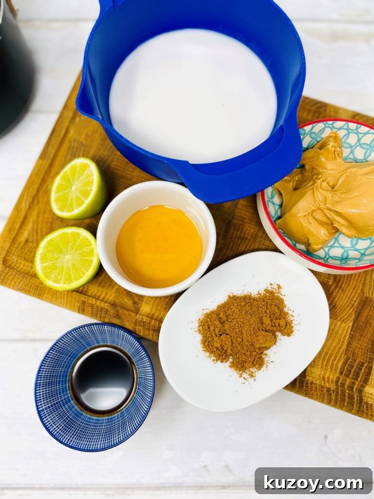 satay stir fry sauce ingredients on a wood board - coconut milk, peanut butter, curry powder, limes, sesame oil, soy sauce