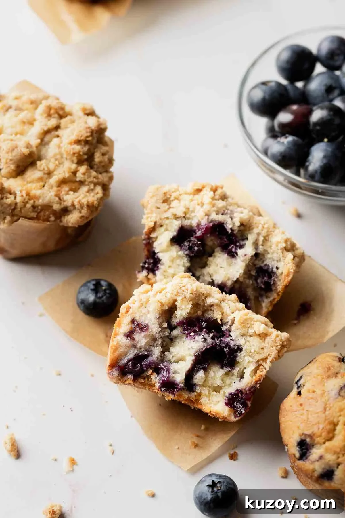 Gluten-Free Blueberry Muffins with Crunchy Streusel Topping 11 Blueberry muffin on parchment paper, split in half to show soft texture filled with juicy blueberries.