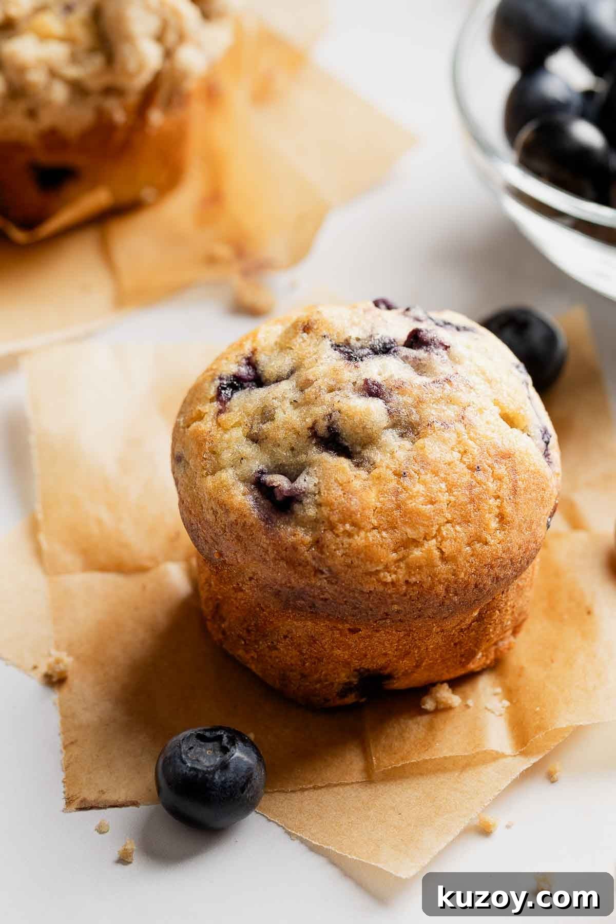 Gluten-Free Blueberry Muffins with Crunchy Streusel Topping 4 Blueberry muffin on parchment paper squares, next to fresh blueberries.
