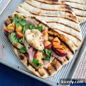 Grilled sourdough flatbread with grilled peaches, burrata, arugula and prosciutto on a baking sheet.