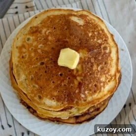 Stack of fluffy sourdough discard pancakes on a plate with a pat of butter on top.
