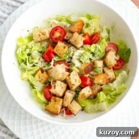 Sourdough croutons in a bowl of green salad with tomatoes, parmesan and dressing.